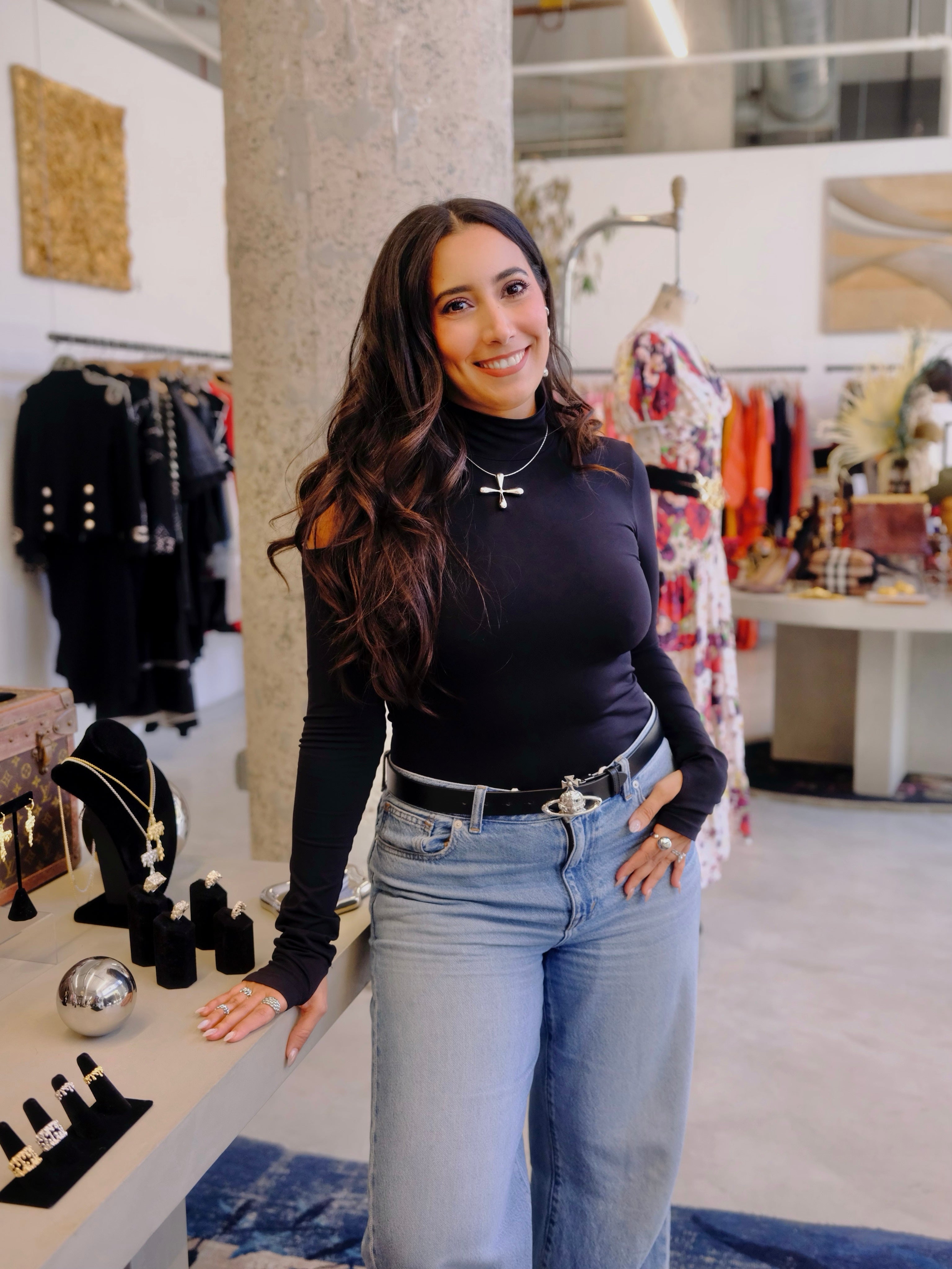 Woman in a black top and jeans standing in a store with clothing and jewelry displays.